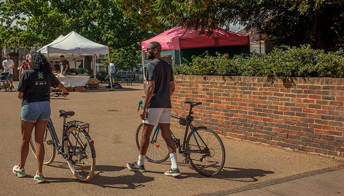 Two people walking their bicycles through a market in London.